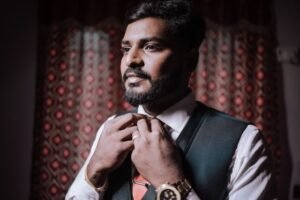 Portrait of an Indian groom adjusting his tie indoors before the wedding ceremony, exuding elegance and focus.